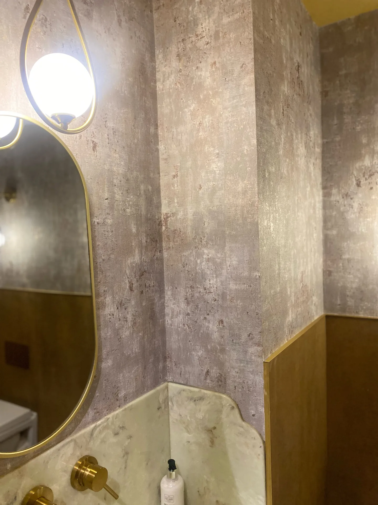 Soft plaster-effect wallpaper in rose and taupe, set off by a brass teardrop wall light and an oval mirror